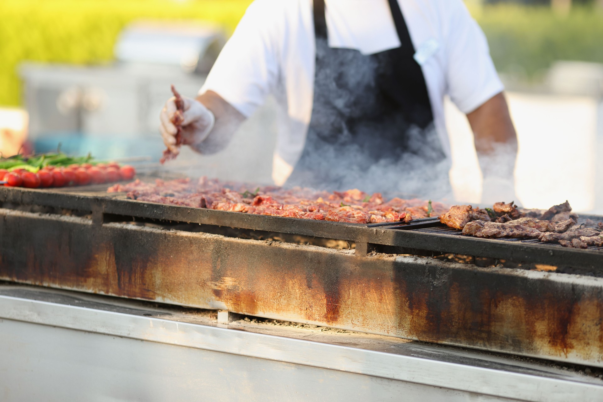 Professional male chef frying fresh meat on grill on open air